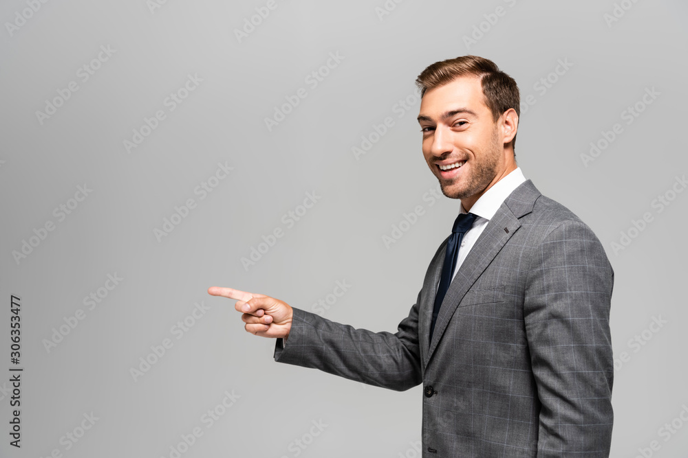 smiling and handsome businessman in suit pointing with finger isolated on grey smiling and handsome businessman in suit pointing with finger isolated on grey