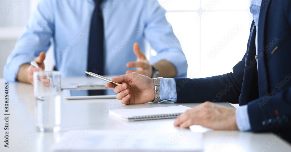 Two unknown businessmen or partners using tablet pc and discussing questions at meeting in modern office, close-up of hands. Group of managers at negotiation or brainstorm. Teamwork, partnership and Two unknown businessmen or partners using tablet pc and discussing questions at meeting in modern office, close-up of hands. Group of managers at negotiation or brainstorm. Teamwork, partnership and