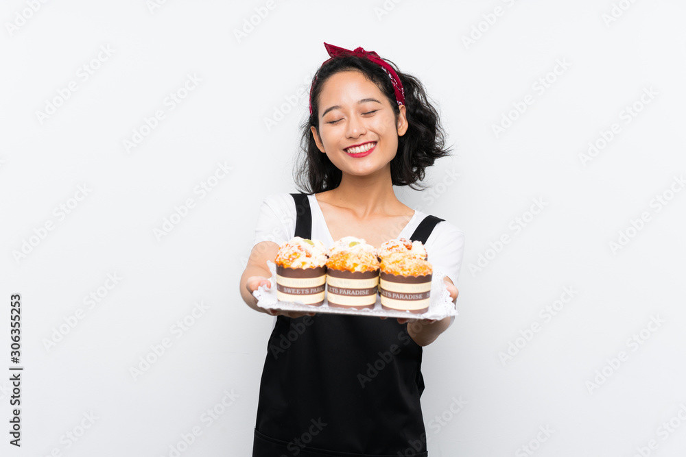 Young asian girl holding lots of muffin cake over isolated white background Young asian girl holding lots of muffin cake over isolated white background