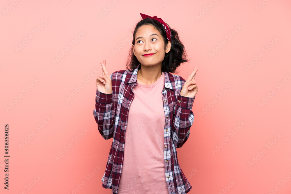 Asian young woman over isolated pink background with fingers crossing and wishing the best