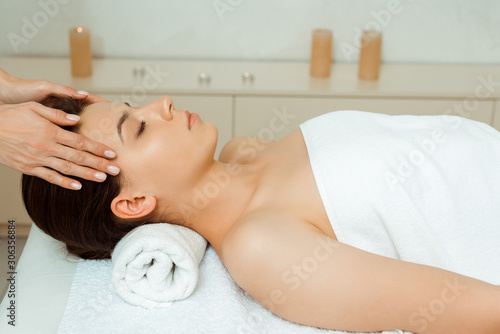 cropped view of masseur doing face massage to attractive woman in spa