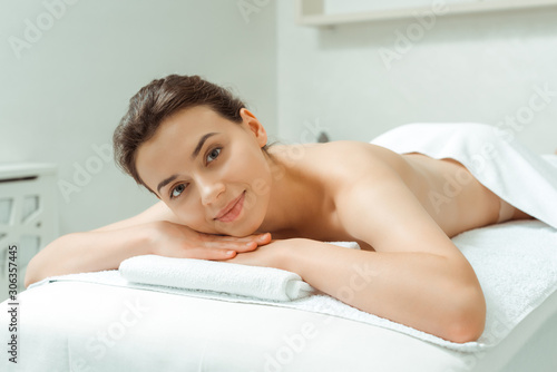 attractive and smiling woman lying on massage table in spa
