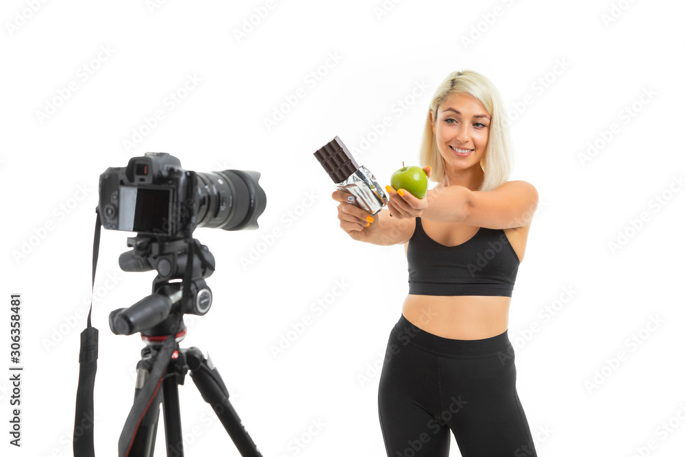 athletic girl in a sports uniform shows apples and chocolate on a camera on a white background