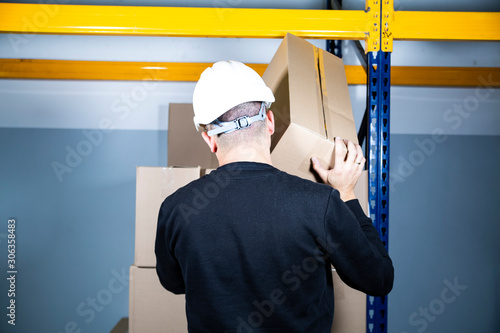 Warehouse work. Man in a hard hat placing a cardboard box on a pile. Safe work in a factory. photo