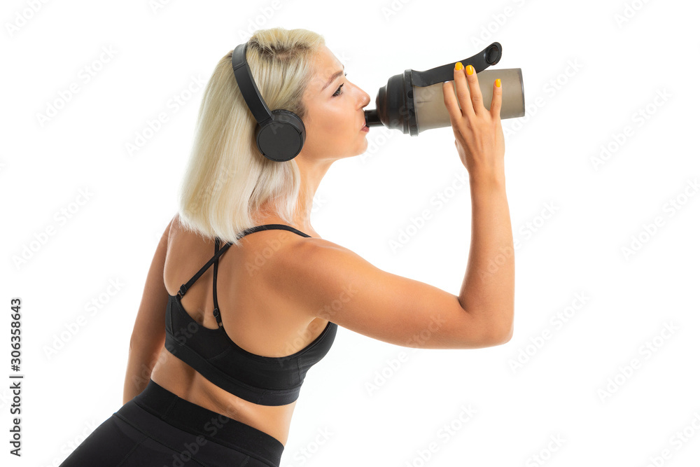 blonde girl in a sports uniform drinks water listens to music on a white background blonde girl in a sports uniform drinks water listens to music on a white background