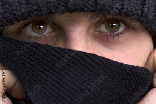 Eyes of young white boy with hat and black scarf. 