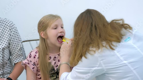 Medicine for children and healthcare concept. Pediatrician looking child girl throat using spatula and lantern, portrait of child. Preventive examination in clinic. Diagnostics tonsillitis or angina.