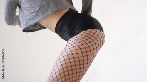 Low angle shot of young seductive female dancer in fishnet tights, shorts and cropped sweatshirt dancing in studio and looking sensually at camera photo