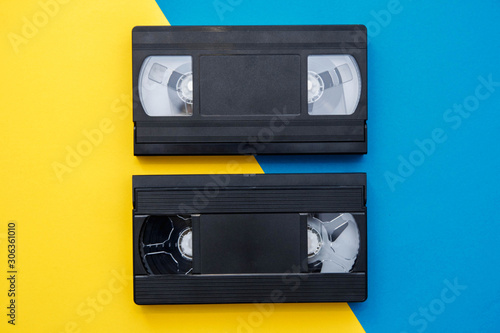 Two video tapes on yellow and blue background. Top view. VHS videotapes. Minimalistic retro concept. Copy, empty space for text