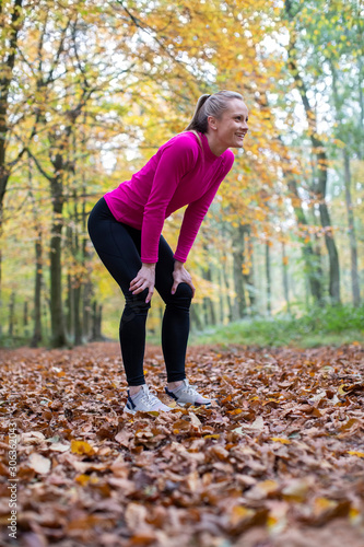 Fototapeta Naklejka Na Ścianę i Meble -  Side View Of Woman On Early Morning Autumn Run Through Woodland Resting After Exercise