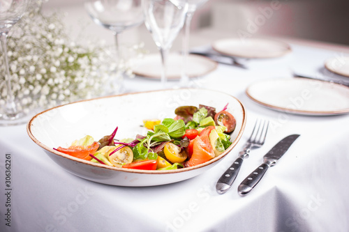 Salmon salad with tomatos in big plate on white table whith fork and knife.