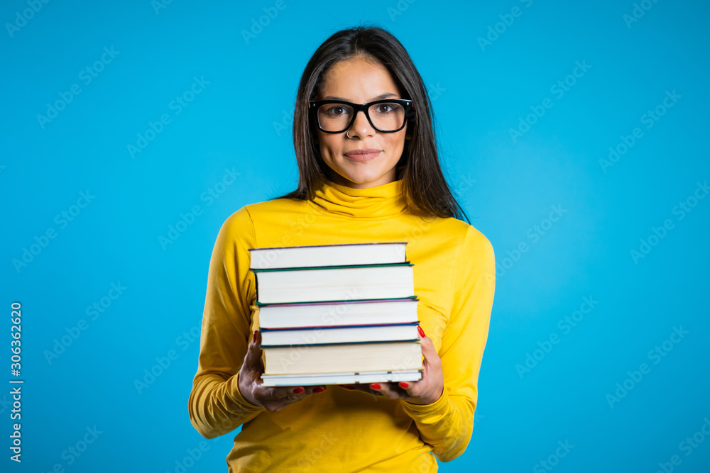 Latin student on blue background in the studio holds stack of university books from library. Guy smiles, he is happy to graduate. Latin student on blue background in the studio holds stack of university books from library. Guy smiles, he is happy to graduate.