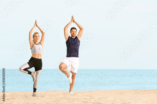 Sporty couple practicing yoga at sea resort