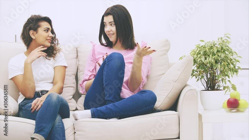 Attractive caucasian girl is telling her afro-american friend an exciting story. Her friend is listening, looking astounded and confused. photo