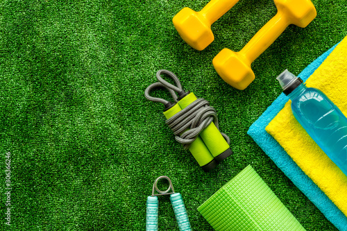 Gym equipment - dumbbells, jump rope - frame on green grass background top-down copy space