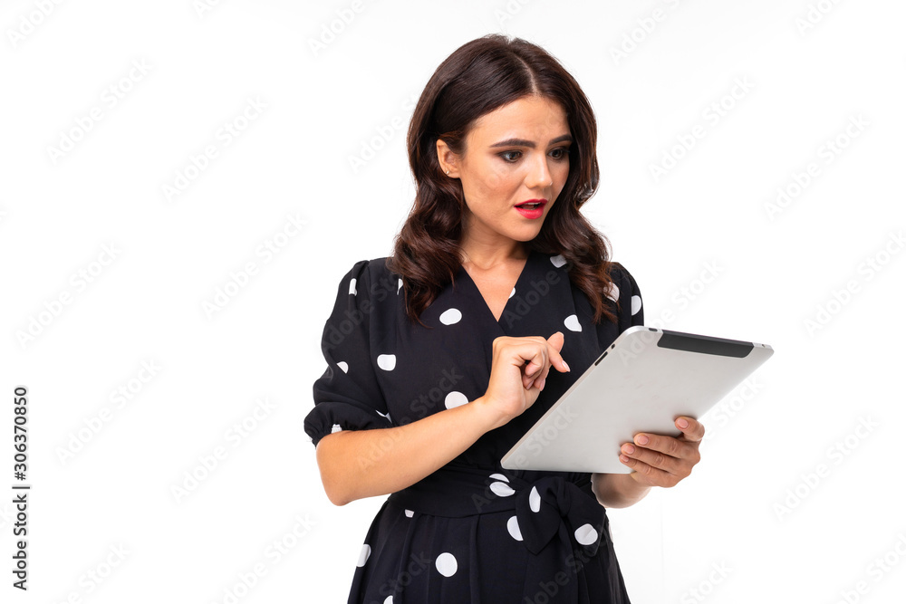 Young caucasian girl with delightful smile, in black and white dress in peas works with a tablet, picture isolated on white background Young caucasian girl with delightful smile, in black and white dress in peas works with a tablet, picture isolated on white background