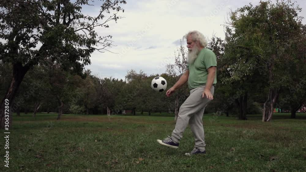 Sportive senior Caucasian man with splendid grey hair, moustache and beard is juggling soccer ball on apple tree garden background. Beautiful portrait of European handsome people in summer leisure. Sportive senior Caucasian man with splendid grey hair, moustache and beard is juggling soccer ball on apple tree garden background. Beautiful portrait of European handsome people in summer leisure.