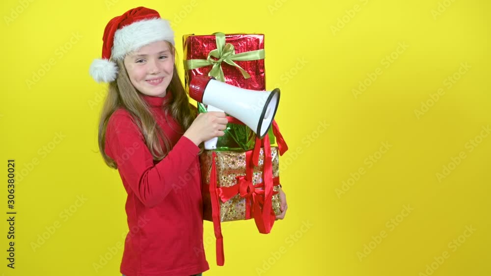Girl in santa claus hat with box boxes in hand shouts into a megaphone, on a yellow studio background. Surprise. Emotions Sales time. 4K UHD Girl in santa claus hat with box boxes in hand shouts into a megaphone, on a yellow studio background. Surprise. Emotions Sales time. 4K UHD