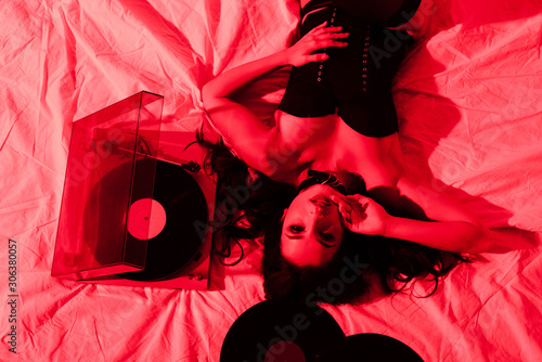 attractive passionate woman lying on bed with vinyl records in red light