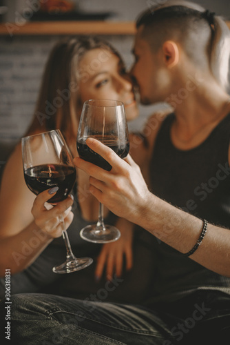 Romantic couple looking at each other smiling ang holding glasses with red wine. Pleasant day with lovely people at home.