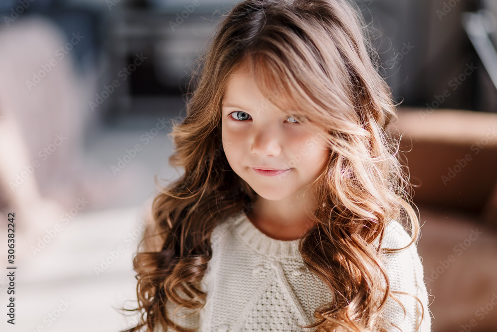 Obraz premium A little girl is sitting on the bed & posing on the eve of the new year 2020. Beautiful baby girl in a gray skirt and a white sweater.
