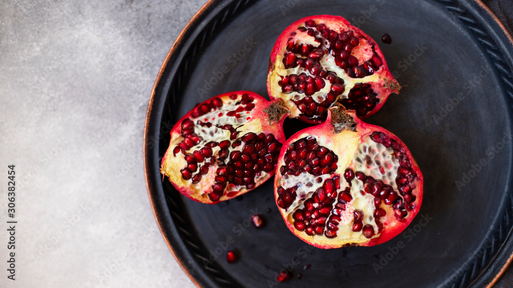 Sliced juicy pomegranate fruits on a vintage metal plate. Top view, gray marble background, copy space