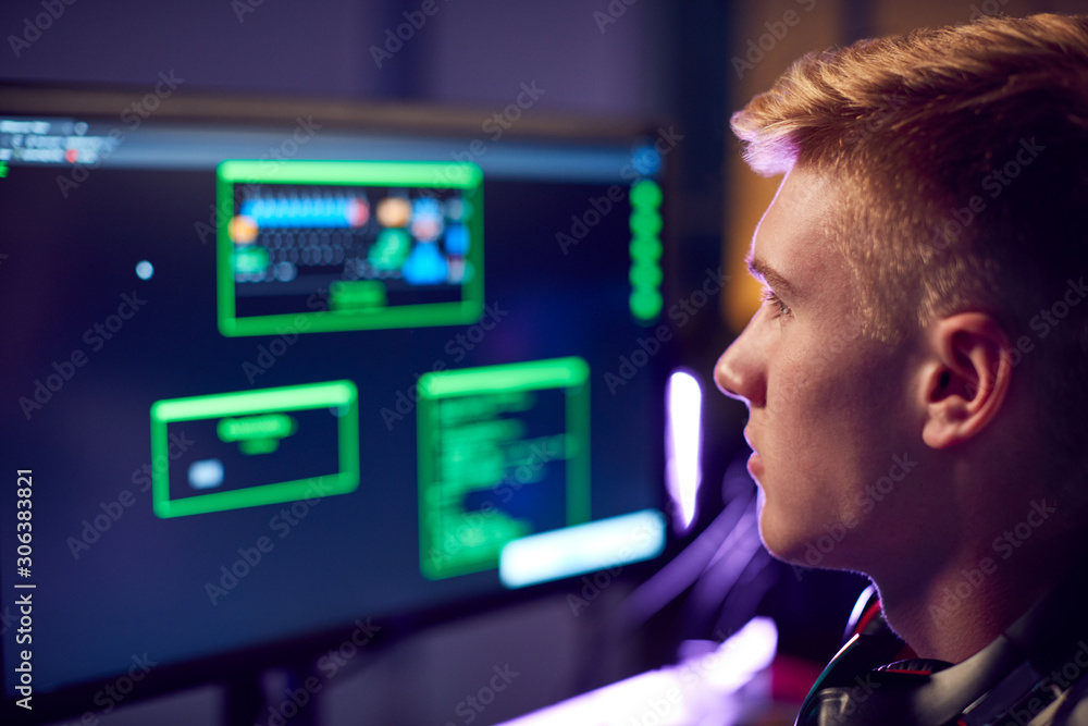 Male Teenage Hacker Sitting In Front Of Computer Screens Bypassing Cyber Security Male Teenage Hacker Sitting In Front Of Computer Screens Bypassing Cyber Security