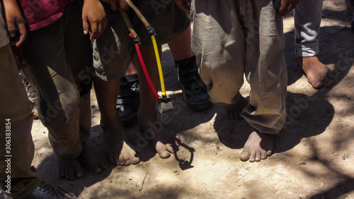 View of feet of indigenous children, with old and worn clothes, on dry and dry ground, with toy in hand