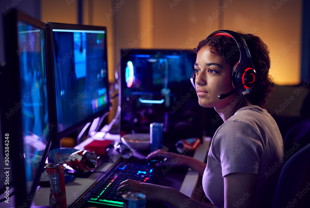 Teenage Girl Wearing Headset Gaming At Home Using Dual Computer Screens Teenage Girl Wearing Headset Gaming At Home Using Dual Computer Screens