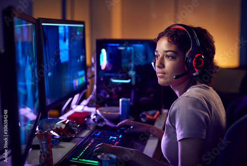 Teenage Girl Wearing Headset Gaming At Home Using Dual Computer Screens