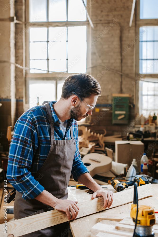 selective focus of bearded woodworker holding plank in workshop selective focus of bearded woodworker holding plank in workshop