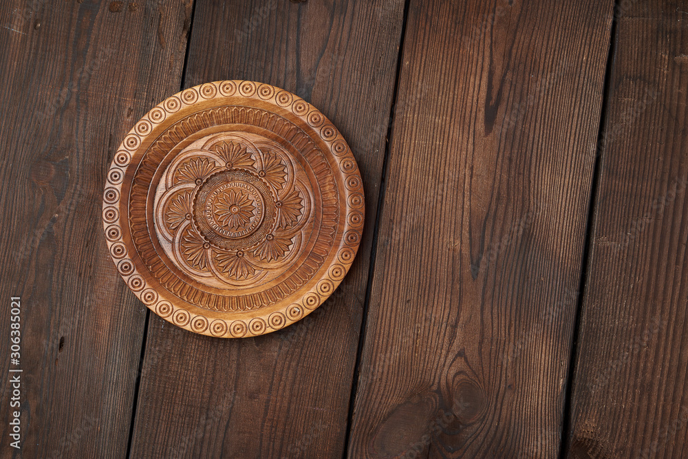 empty round brown carved decorative plate standing on a wooden background empty round brown carved decorative plate standing on a wooden background