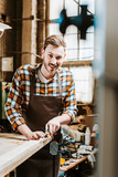selective focus of cheerful woodworker holding chisel while carving wood in workshop