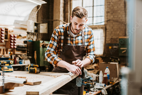 Valokuva Selective focus of bearded woodworker holding chisel while carving wood in works