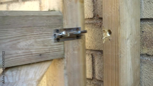 Slow motion close shot of a man’s hand unbolting a wooden gate, opening it to pass through, then bolting it.