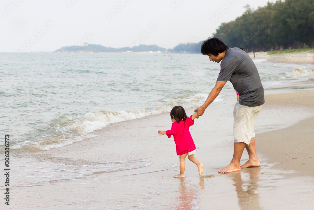 Portrait image of Asian Father with his daughter are hand in hand and walking on the beach at the sea. Summer season. Father's day and family concept. Portrait image of Asian Father with his daughter are hand in hand and walking on the beach at the sea. Summer season. Father's day and family concept.