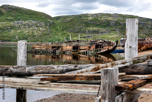 Russia, Arctic, Kola Peninsula, Barents Sea, Teriberka: Rusty abandoned fishing boats shipwreck at low tide near the traditional fishing harbor of the old Russian settlement small fishing village.