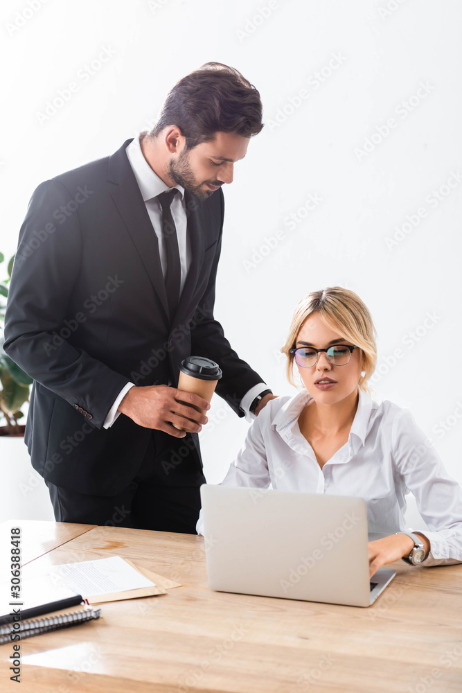 Businessman with coffee looking at colleague working with laptop Businessman with coffee looking at colleague working with laptop