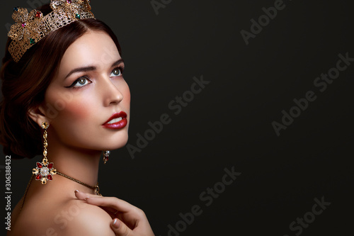 Beautiful girl with red lipstick in golden crown and earrings on dark background