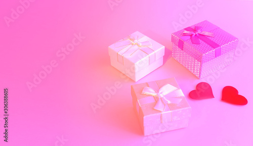 Three gift boxes with ribbon bows and two red hearts on a pink background. Valentine's Day. Birthday.Wedding.Copyspace