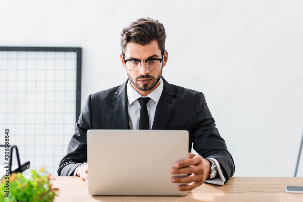 Handsome businessman looking at camera while using laptop Handsome businessman looking at camera while using laptop