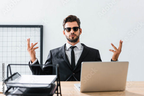 Handsome businessman in sunglasses gesturing at office table