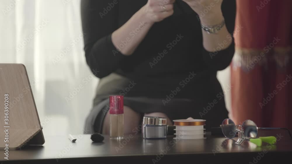Close-up of a table with cosmetics. Unrecognizable Caucasian woman sitting and doing makeup. Fashion, beauty, face care, skin care.