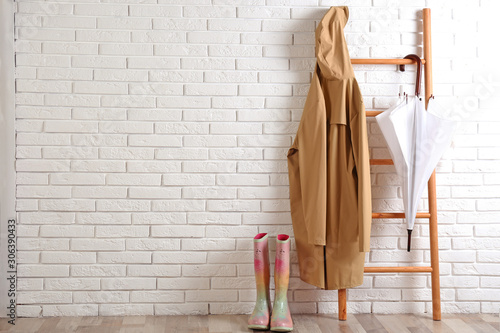 Umbrella, raincoat and rubber boots near white brick wall. Space for text photo