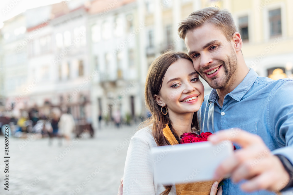 selective focus of smiling tourists taking selfie with smartphone on street selective focus of smiling tourists taking selfie with smartphone on street