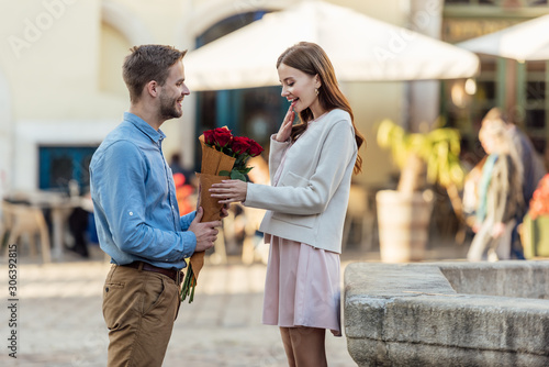 happy man presenting bouquet of roses to beautiful girlfriend on street