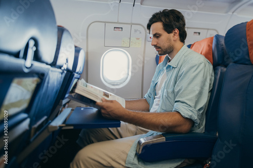 The guy flies in an airplane with a magazine in his hands