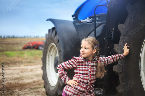 Фотография Cute girl near the modern tractor in the field.
