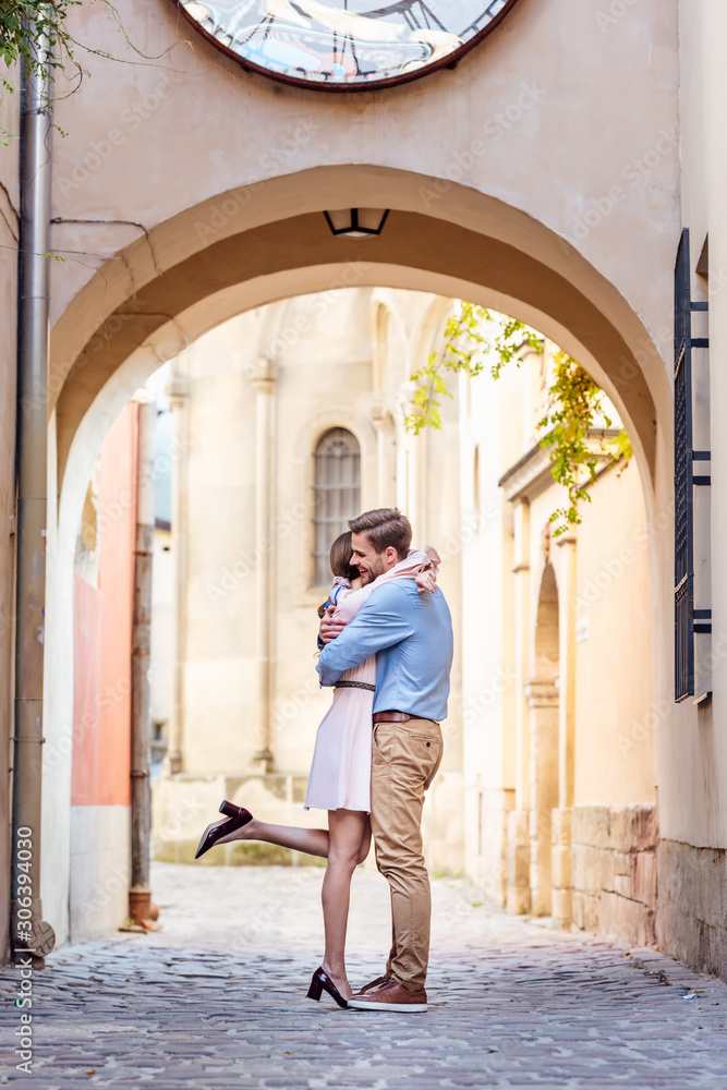 couple of happy young tourists embracing while standing under arch on street