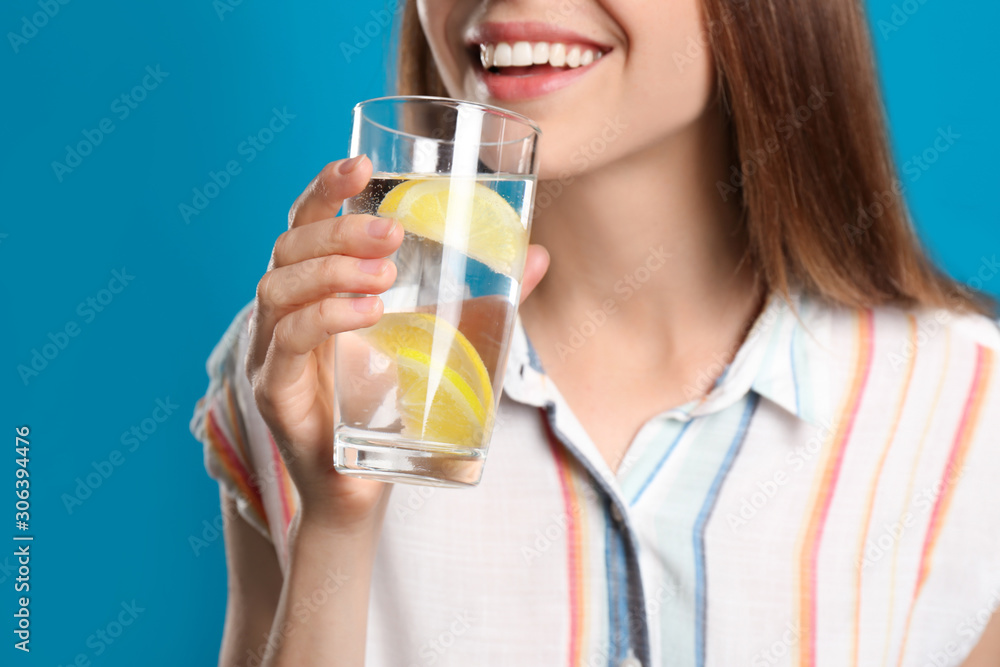 Young woman drinking lemon water on light blue background, closeup Young woman drinking lemon water on light blue background, closeup